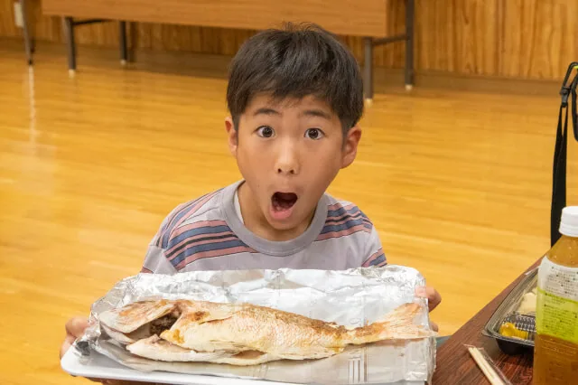 魚の浜焼きを手にする子どもの主催参考写真